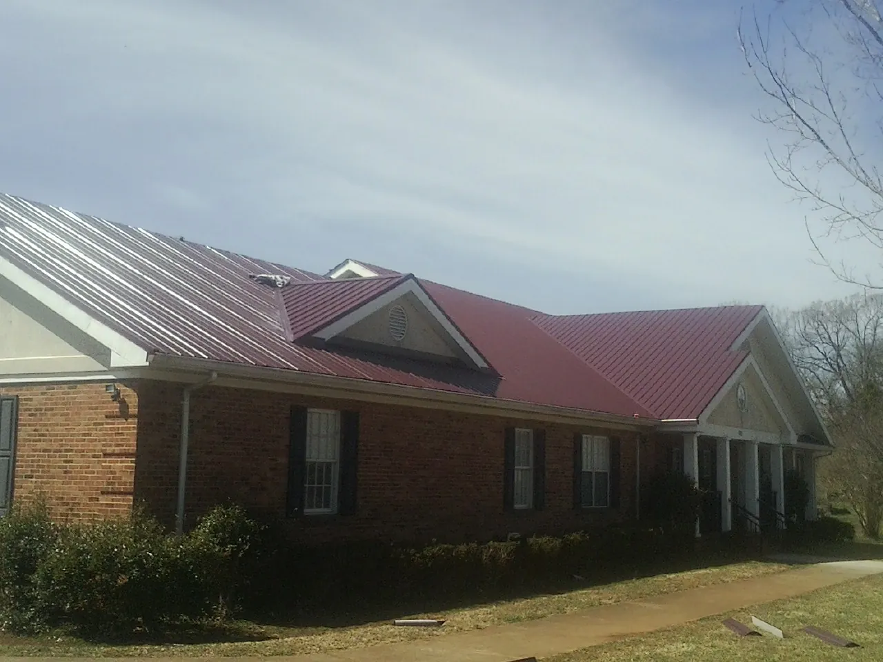 Red metal roof with gabled entries on a long brick building, from a Hail Damage Roof Repair job in Boston