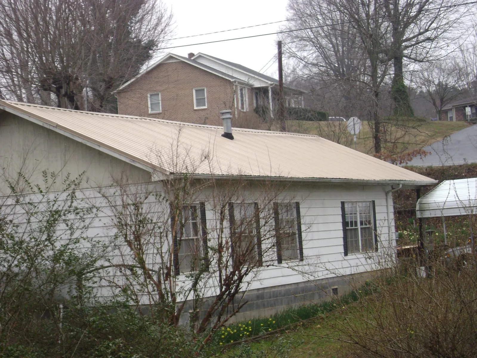 Tan metal roof on a white sided house set into a hillside — Commercial Roofing by Roofing Brothers in Boston